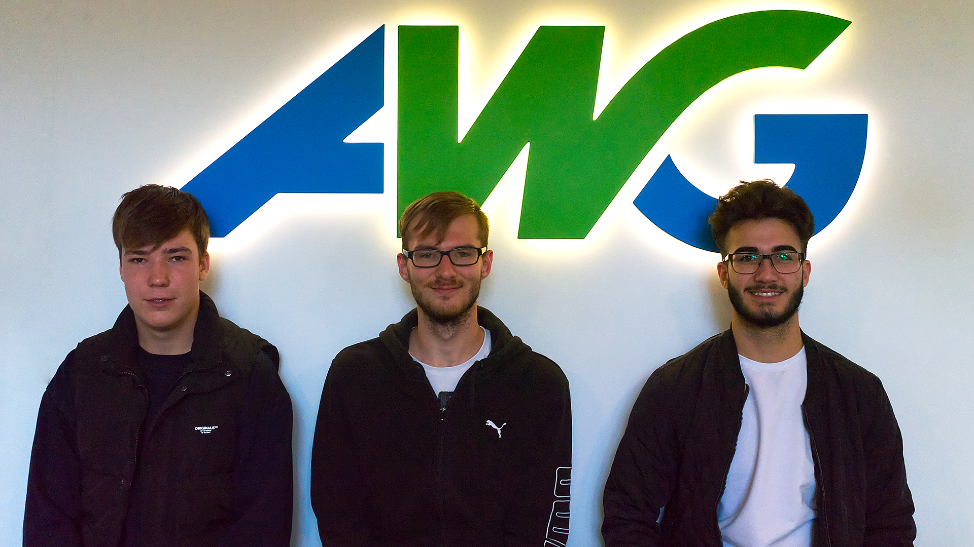 Drei Personen vor einem AWG-Logo.