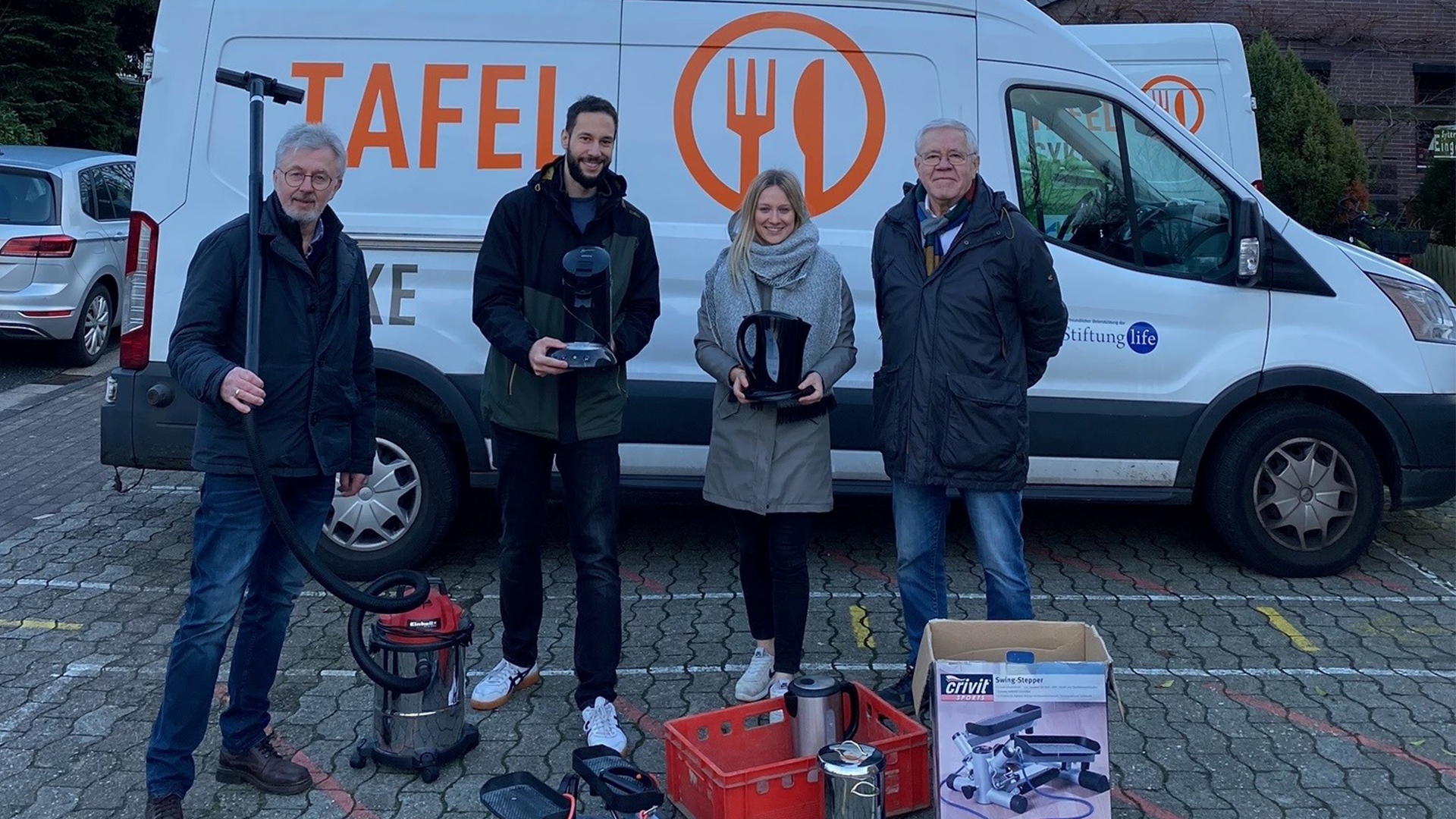 Vier Personen vor einem Fahrzeug der Tafel mit Elektrogeräten in der Hand.