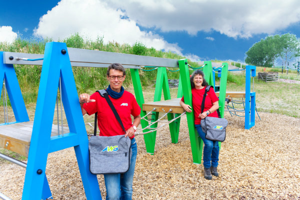 Renate Meyer und Silke Stolle stehen in roter Dienstkleidung an dem AWG-Klettergerüst am Eingang des Utkieks.