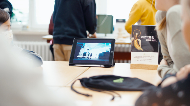 Kinder sitzen an einem Tisch und schauen einen Film auf einem Tablet